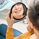 Senior patient examining her smile in mirror at Albanian dental clinic.